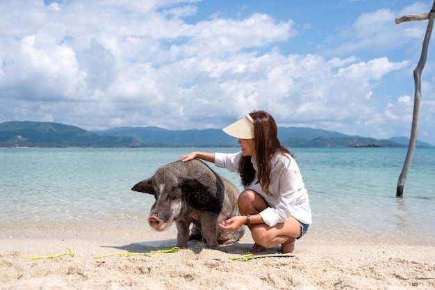 A beautiful young asian woman playing with a pig by the sea on the pig island