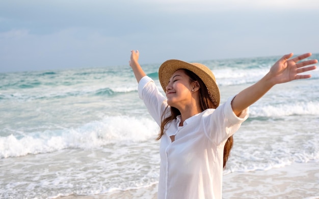 A beautiful young asian woman raising hands while strolling on the beach with the sea and blue sky background