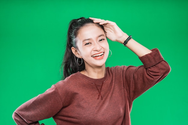 Beautiful young Asian woman smiling while holding over the head isolated on green background