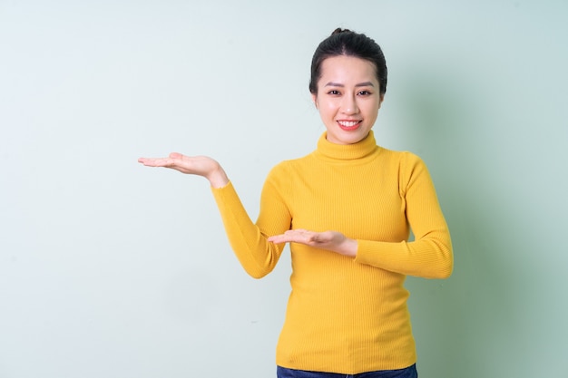 Beautiful young Asian woman wearing sweater on green background