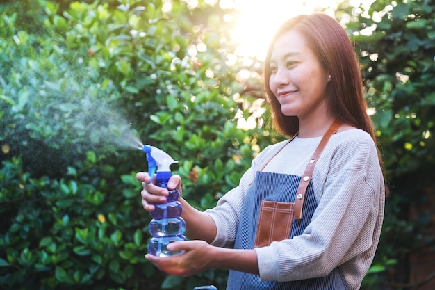 A beautiful young asian woman with apron watering plant by foggy spray in garden