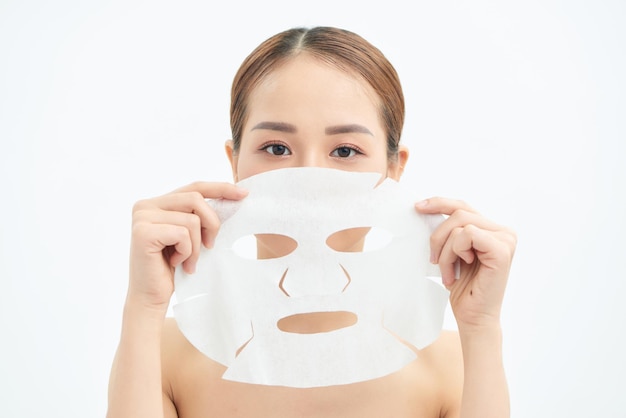 Beautiful young Asian woman with paper sheet mask holding hands on her face on white background