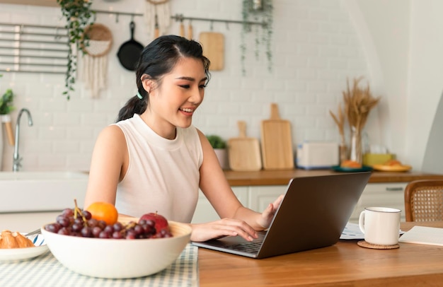 Beautiful young asian woman working on laptop computer while sitting at the kitchen room background