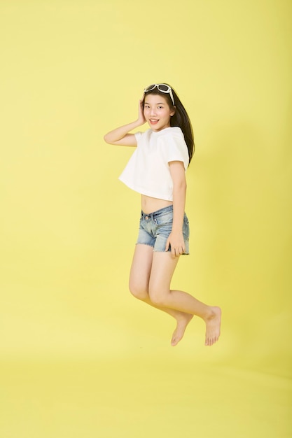 Beautiful young Asian women with sunglasses on her head jumping on yellow background