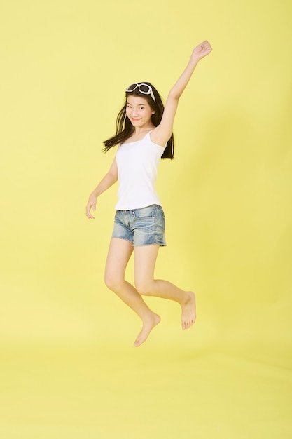 Beautiful young Asian women with sunglasses on her head jumping on yellow background