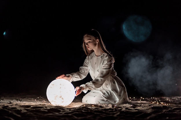 Beautiful young attractive girl on a night beach with sand and stars holds the moon in her hands