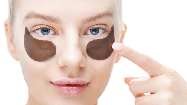 Beautiful young blond woman shows fingers on eye patches of black color on a white background in isolation. Care and face masks