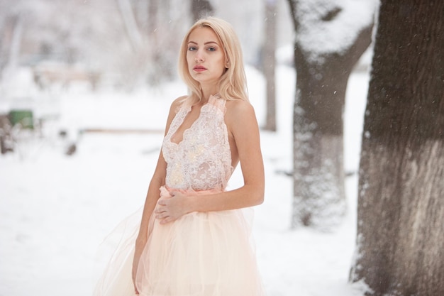 A beautiful young blond woman in a white dress posing in a snowy winter park. Soft focus. Selective focus