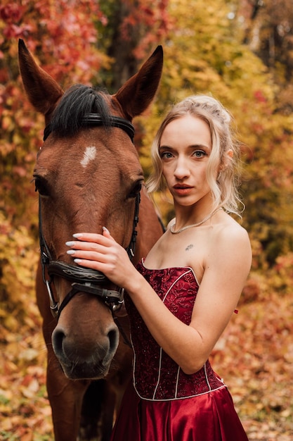 Beautiful young blonde in a burgundy dress hugs a bay horse