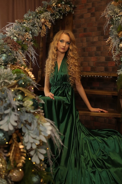 beautiful young blonde girl in a chic green dress on the stairs decorated for christmas new year