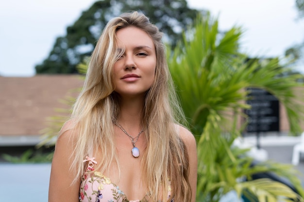 Beautiful young blonde in a top with long hair and smooth clean soft skin natural beauty daylight pendant on neck accessory posing with palm leaf