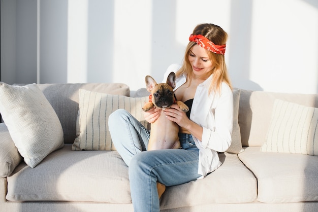 Beautiful young blonde woman playing with her dog at home, smiling