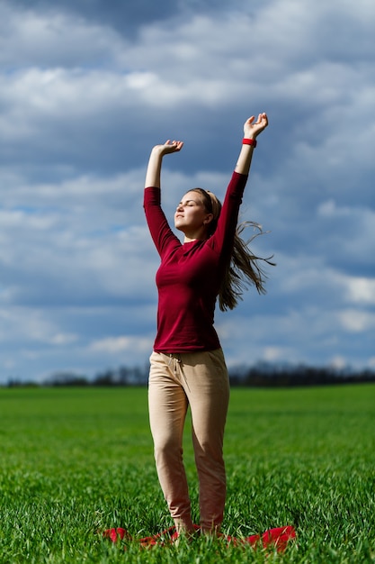 Beautiful young blonde woman stands on green grass in a park. Blue sky with clouds. The girl smiles and enjoys a good day.