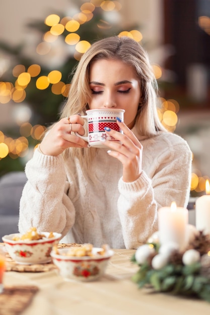 A beautiful young blonde woman tastes christmas punch tea mulled wine or coffee