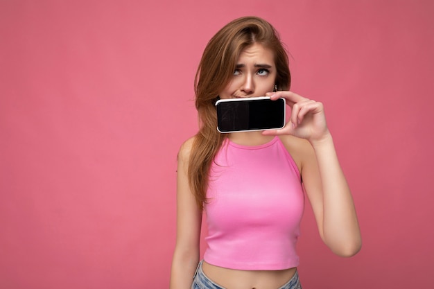 Beautiful young blonde woman wearing pink top poising isolated on pink background with empty space