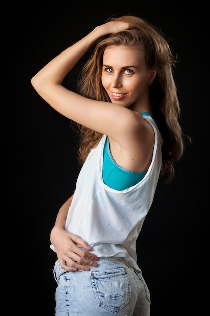 Beautiful young blonde woman in white top in denim shorts smiling and posing