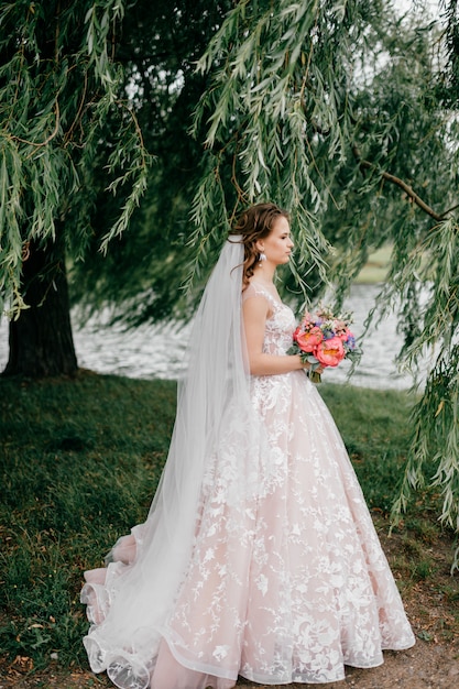 Beautiful young bride in white wedding dress posing outdoor with bouquet of flowers