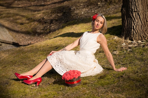 Beautiful young bride with red flowers sitting on the grass at the park