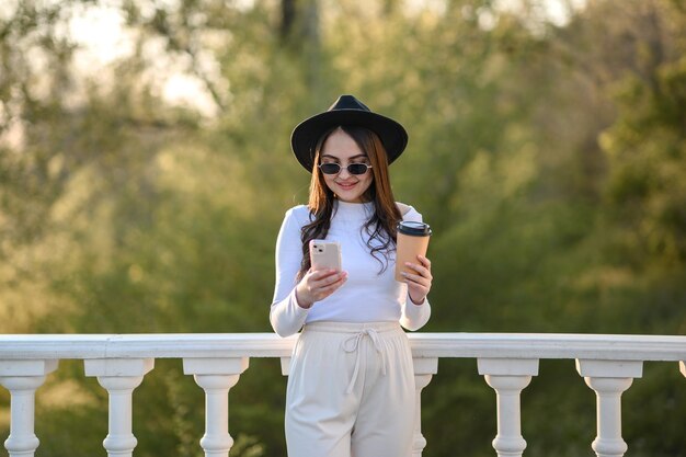 Beautiful young brunette girl in a hat with glasses and with a phone in her hands