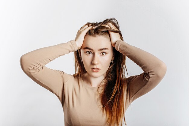 Beautiful young brunette girl in horror holding her head isolated on white