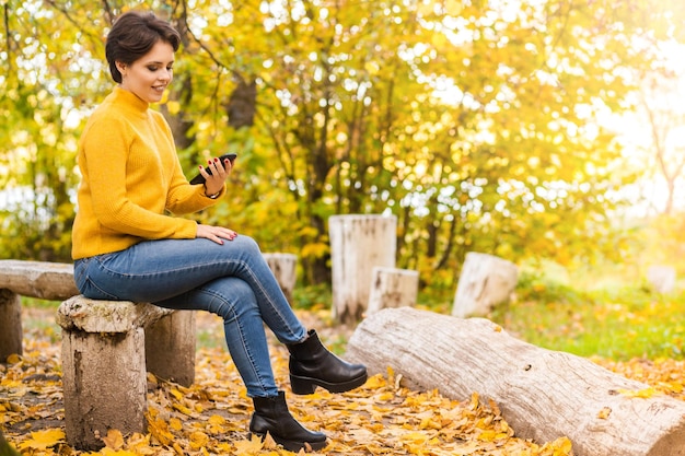 Beautiful young brunette girl posing in the autumn park with a mobile phone in her hands