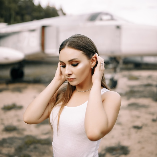 Beautiful young brunette girl stands on the background of old military aircraft.