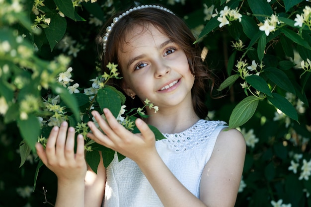 Beautiful young brunette girl with dark long hair on the background of foliage and flowers in the park child portrait european appearance. High quality photo