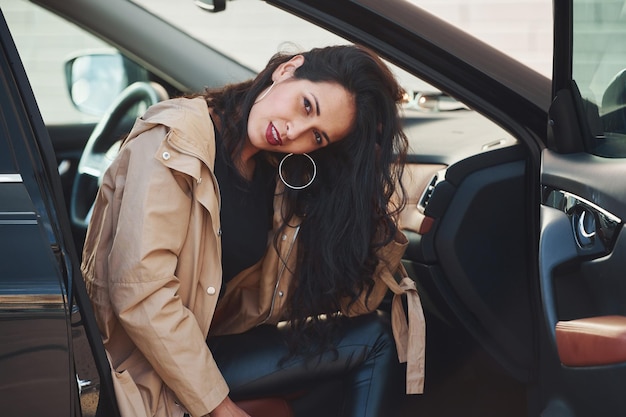 Beautiful young brunette with curly hair sitting inside of modern car