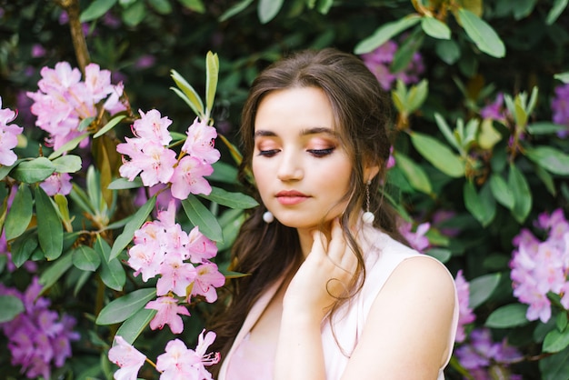 beautiful young brunette with a smile and big brown eyes in blooming gardens of pink rhododendrons closed her eyes