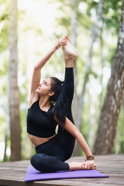 Beautiful young brunette woman in black sportswear practices yoga doing Surya Yantrasana exercise