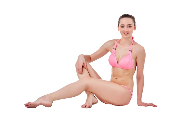 Beautiful young brunette woman in pink swimwear sitting and isolated on white background