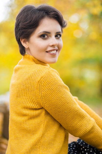 Beautiful young brunette woman in a yellow knitted sweater with a short haircut smiles and looks at