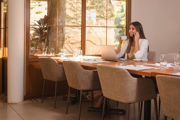 Beautiful young business girl talking on the phone while having a coffee in the restaurant