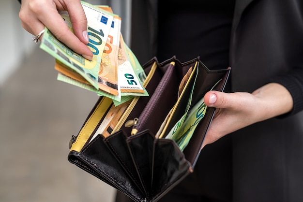 Beautiful young business lady in stylish clothes holding a big purse with euro banknotes