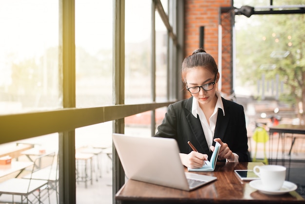 Beautiful young business woman sitting at table and taking notes. In cafe