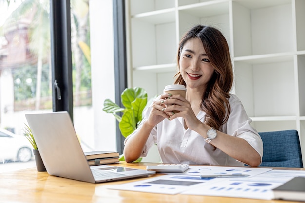 Beautiful young businesswoman drinking hot coffee. A businesswoman drinks coffee during the day, she is checking documents from the finance department. Asian business woman concept.