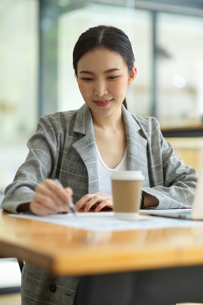 Beautiful young businesswoman using laptop and doing some paperwork