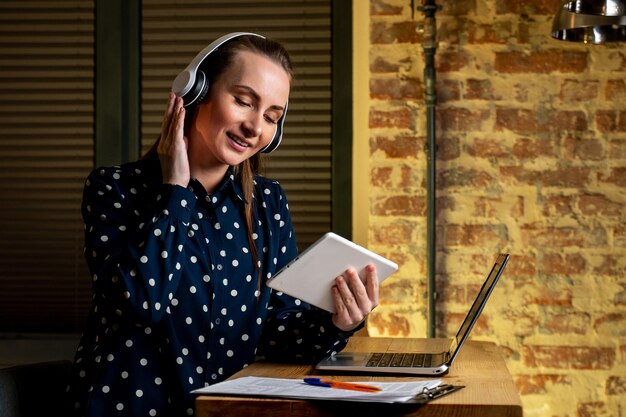 Beautiful young businesswoman wearing headphones is sitting at an office tablet placed in the office