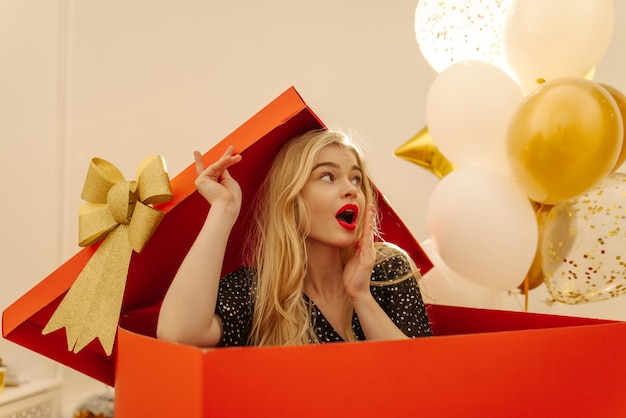 Beautiful young caucasian blonde girl looks away with surprise while sitting in big red box Lifestyle female beauty concept