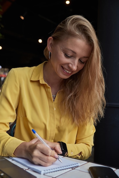 Beautiful young caucasian business woman sitting indoors writing notes in notebook