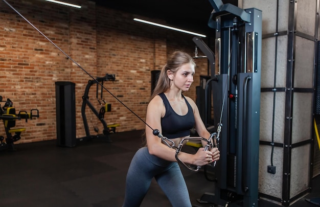 Beautiful young Caucasian female athlete exercising with cable crossover machine in fitness Gym.