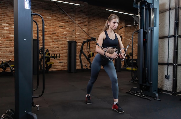 Beautiful young Caucasian female athlete exercising with cable crossover machine in fitness Gym.