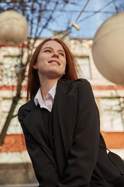 Beautiful young caucasian woman in coat with long hair sitting outdoors at park