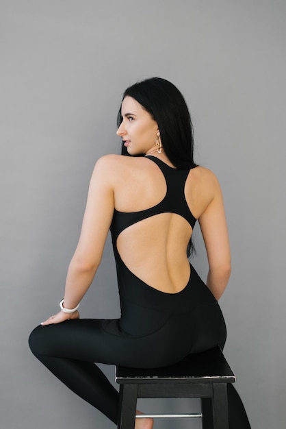 Beautiful young Caucasian woman is sitting on a chair in a black sports suit