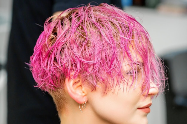 Beautiful young caucasian woman receiving new short pink hairstyle in hairdresser salon