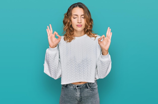 Beautiful young caucasian woman wearing casual winter sweater relax and smiling with eyes closed doing meditation gesture with fingers yoga concept