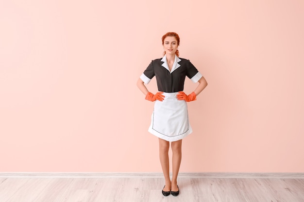 Photo beautiful young chambermaid near color wall