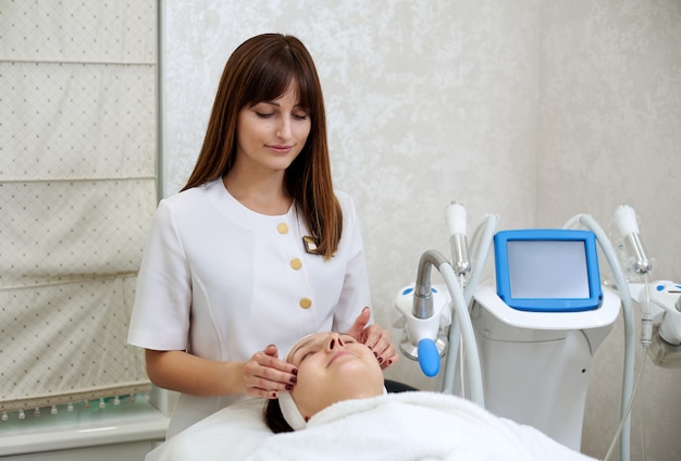 Beautiful young cosmetologist doing facial massage to a young woman in beauty salon