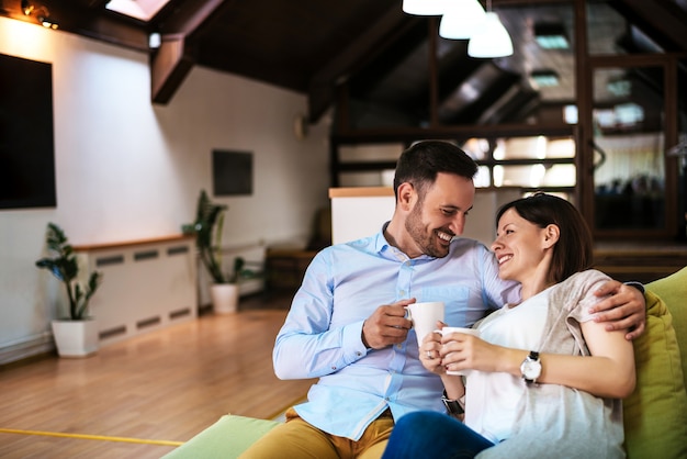 Beautiful young couple drink coffee while sitting on a sofa and looking each other