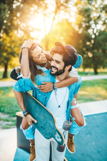 Beautiful young couple enjoying, kissing and hugging outdoors in city skateboarding park.